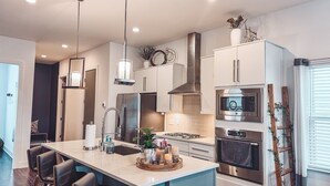 Een moderne keuken met roestvrijstalen apparatuur, een centraal eiland, hanglampen en uitzicht op de eethoek.