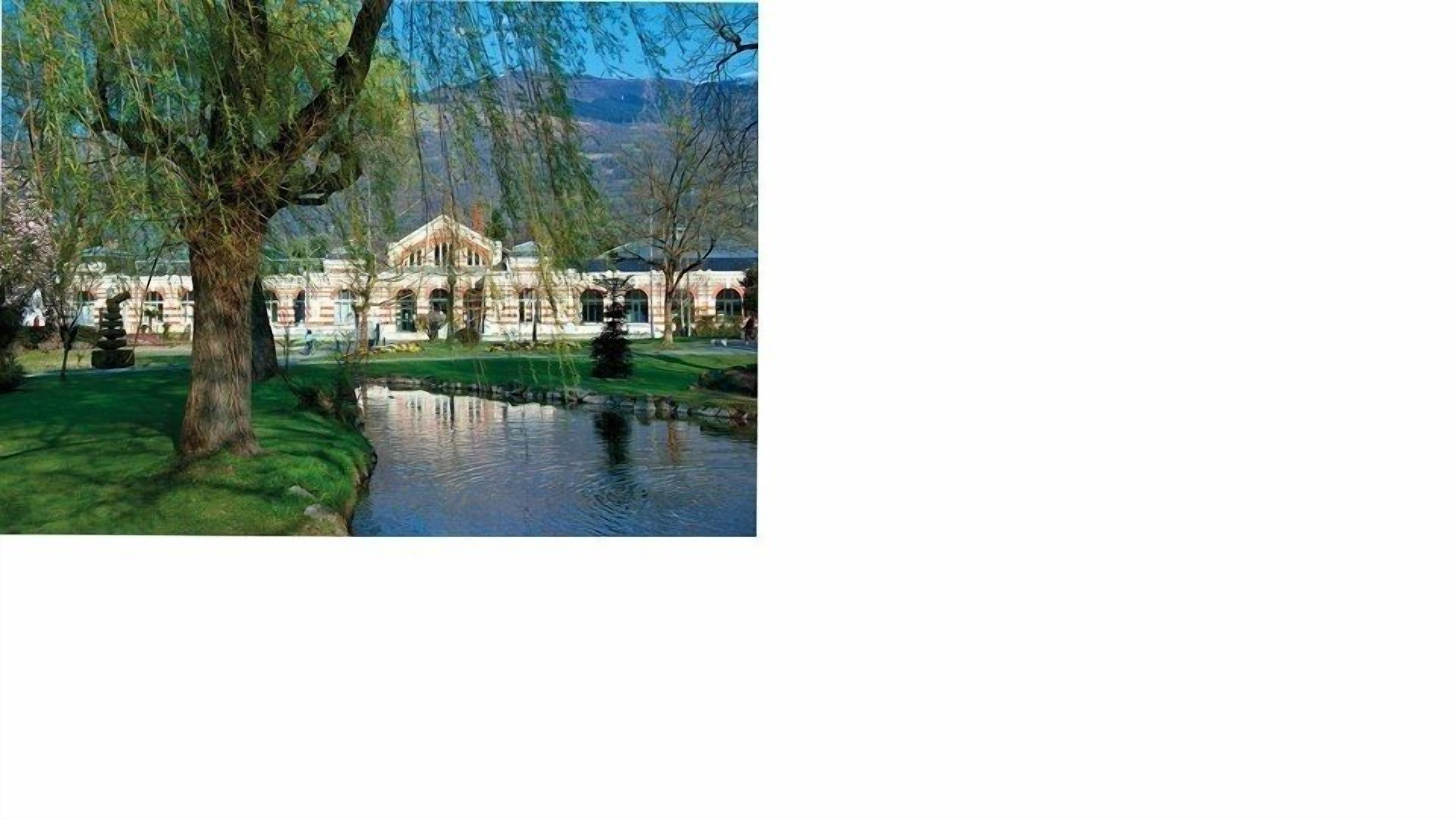 A building with a classical architectural style, a pond, and a large tree in a park setting.