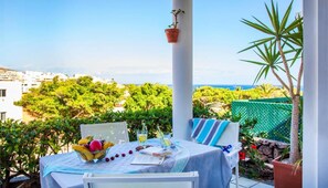 A table set with a fruit bowl, glasses, and a book, overlooking a scenic view with buildings and greenery. - Casa Cuba (Morro Jable)
