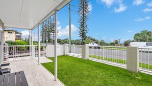 A covered outdoor area with a grassy lawn, white metal fence, and a street view with parked cars.