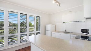 A modern kitchen with white cabinetry, a built-in microwave, and a window with metal bars.