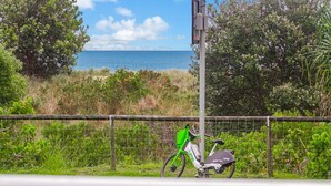 A lime-colored electric bike parked beside a fence with a view of the ocean and greenery.