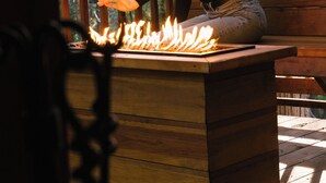A person sitting on a wooden bench outdoors with a fire in front of them. - Idyllbrook: Mission-style gem with a screened BrookHouse gazebo & EV charger. (Idyllwild-Pine Cove)