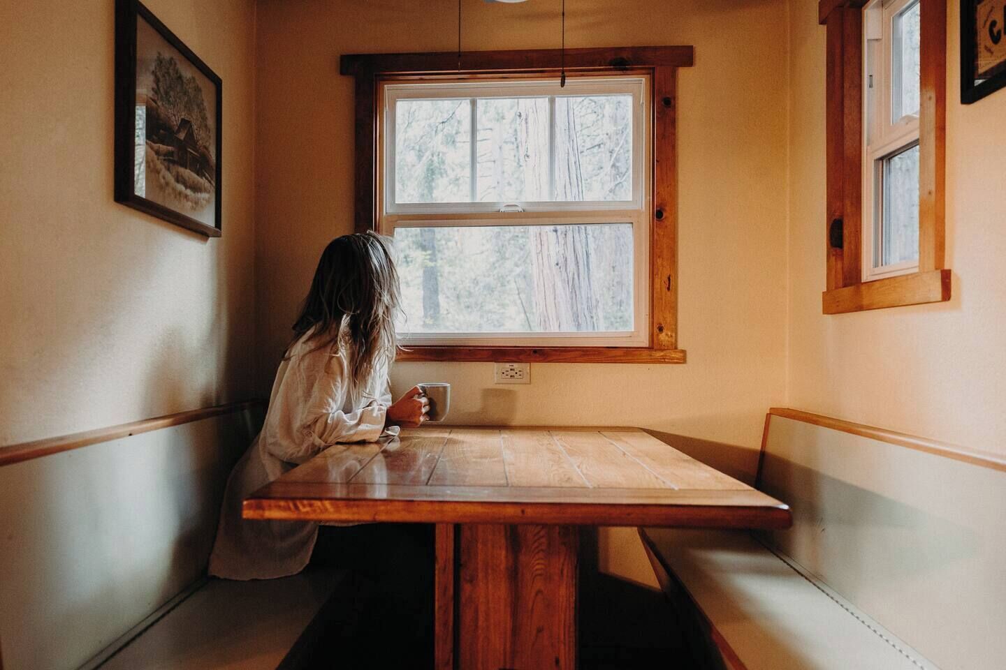 Une personne est assise à une table en bois près d’une fenêtre, d’où l’on peut voir des arbres.