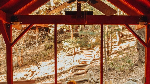 A wooden cabin with a large window, a ceiling fan, and a sofa with cushions. - Idyllbrook: Mission-style gem with a screened BrookHouse gazebo & EV charger. (Idyllwild-Pine Cove)