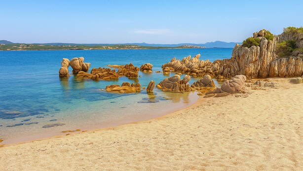 A beach with clear water, rocky formations, and a distant mountain range.