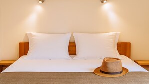 A neatly made bed with white linens, a wooden headboard, and a straw hat on the bed.
