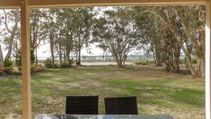 A covered outdoor seating area with a view of a beach and trees. - Riverside - Burrum Heads- Riverfront - 3BR - River Fishing... (BURRUM HEADS)