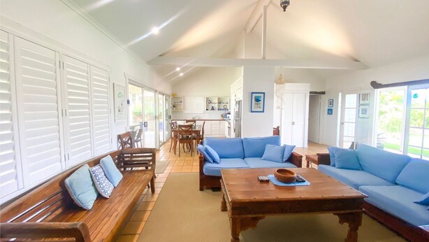 A spacious living area with a large blue sofa, wooden benches, and a wooden coffee table. - Riverside - Burrum Heads- Riverfront - 3BR - River Fishing... (BURRUM HEADS)