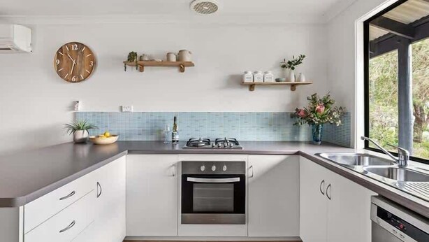 A modern kitchen with white cabinets, a built-in oven, a sink, and a clock on the wall. - Cormorant Cottage—Garden Beach Abode w/ Game Room (Dunsborough)
