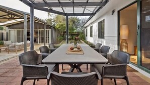 A covered patio with a dining table and chairs, a glass door entrance, and a view of the surrounding garden. - Cormorant Cottage—Garden Beach Abode w/ Game Room (Dunsborough)
