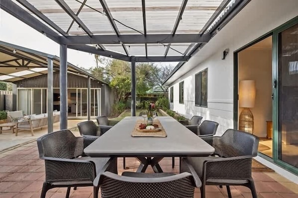 Un patio cubierto con una mesa y sillas de comedor, una puerta de vidrio y vistas al jardín circundante.