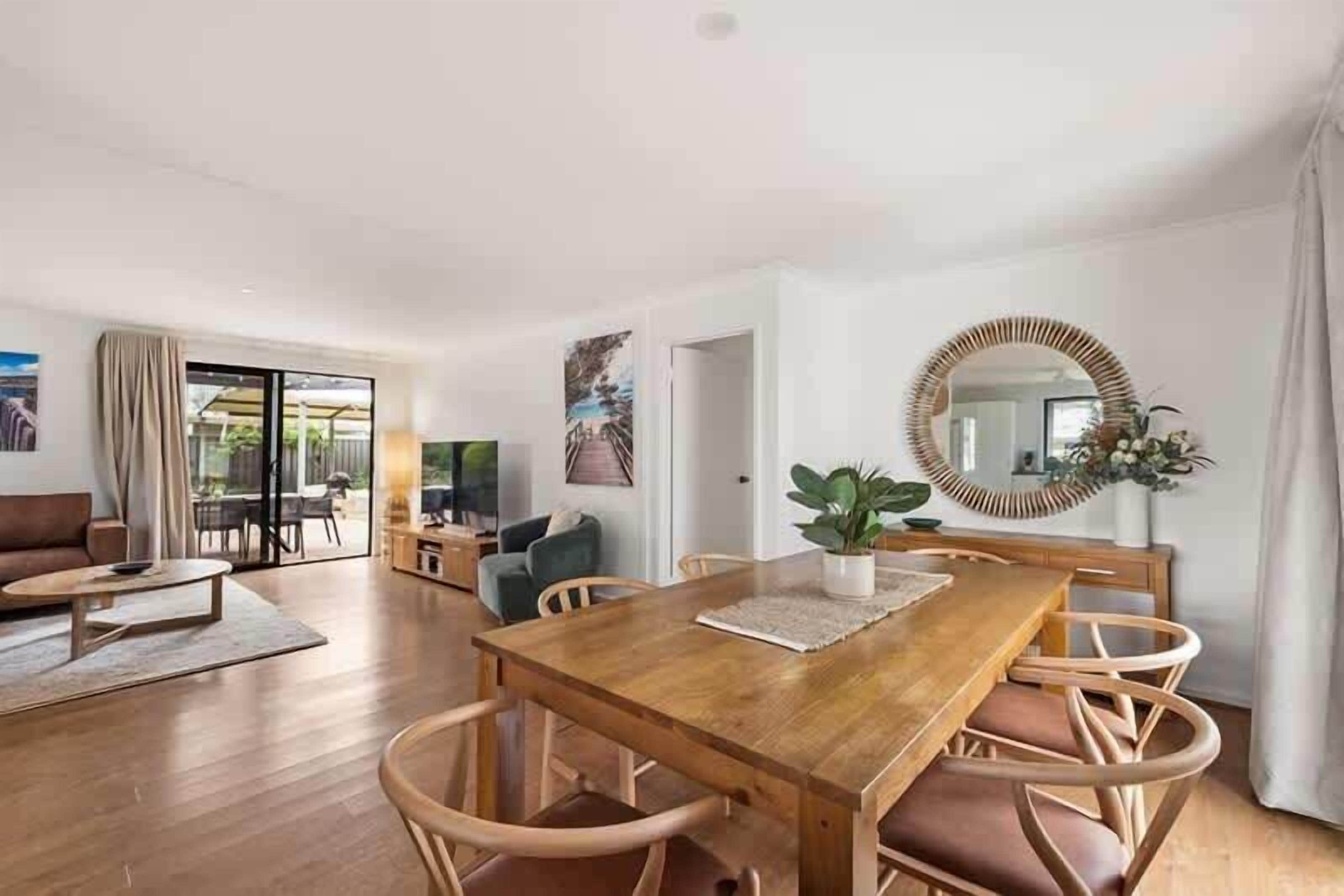 Un vaste espace de vie comprenant une table à manger en bois, des chaises en osier et un grand miroir.