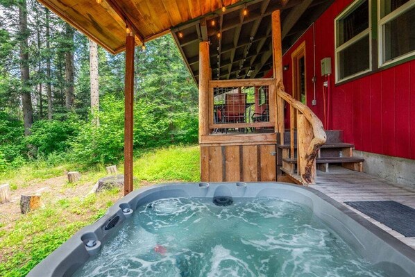 A hot tub with a wooden deck and a red building in the background.