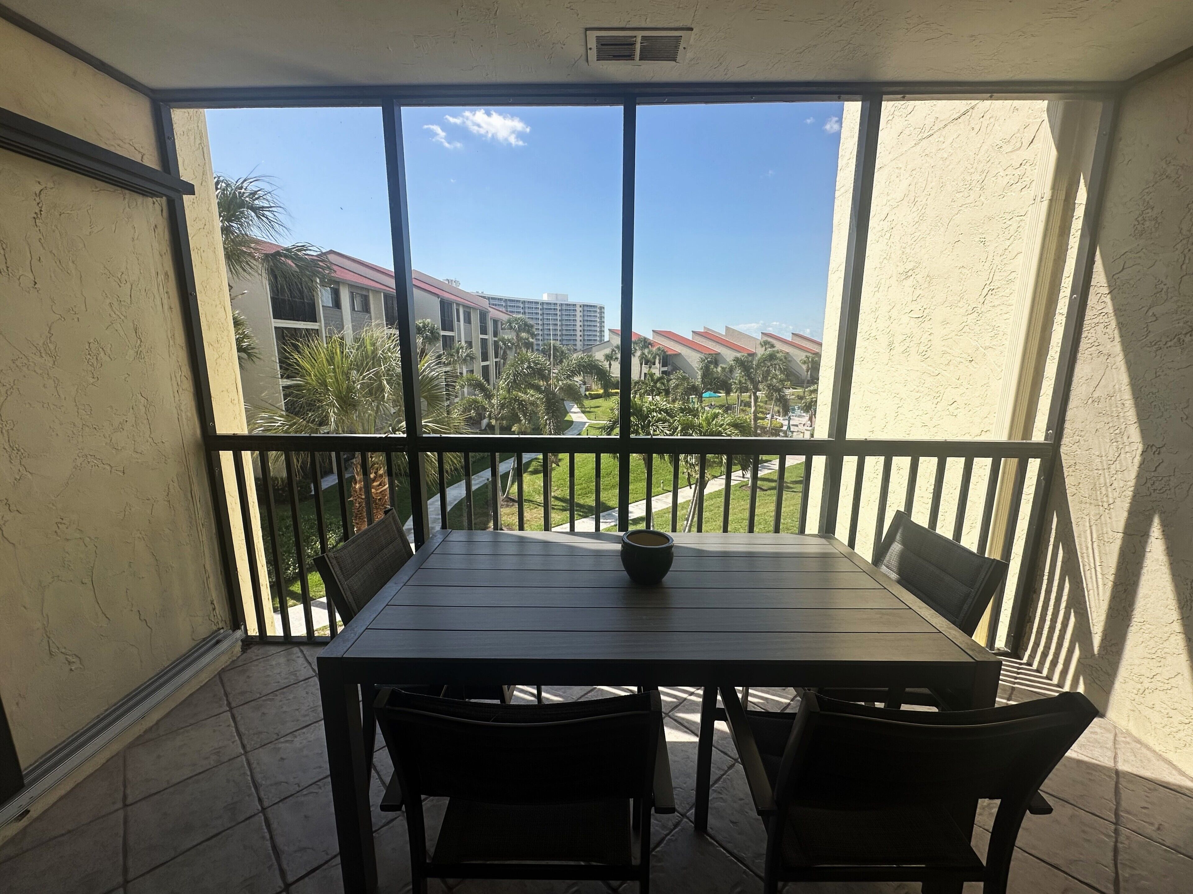 A balcony with a table and chairs, overlooking a landscaped area with buildings in the background.