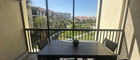 A balcony with a table and chairs, overlooking a landscaped area with buildings in the background.