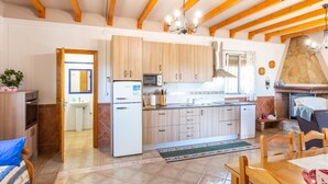 A kitchen with wooden cabinets, a refrigerator, a microwave, and a stone fireplace. - Cosy cottage with pool, garden and wifi (Dúrcal)