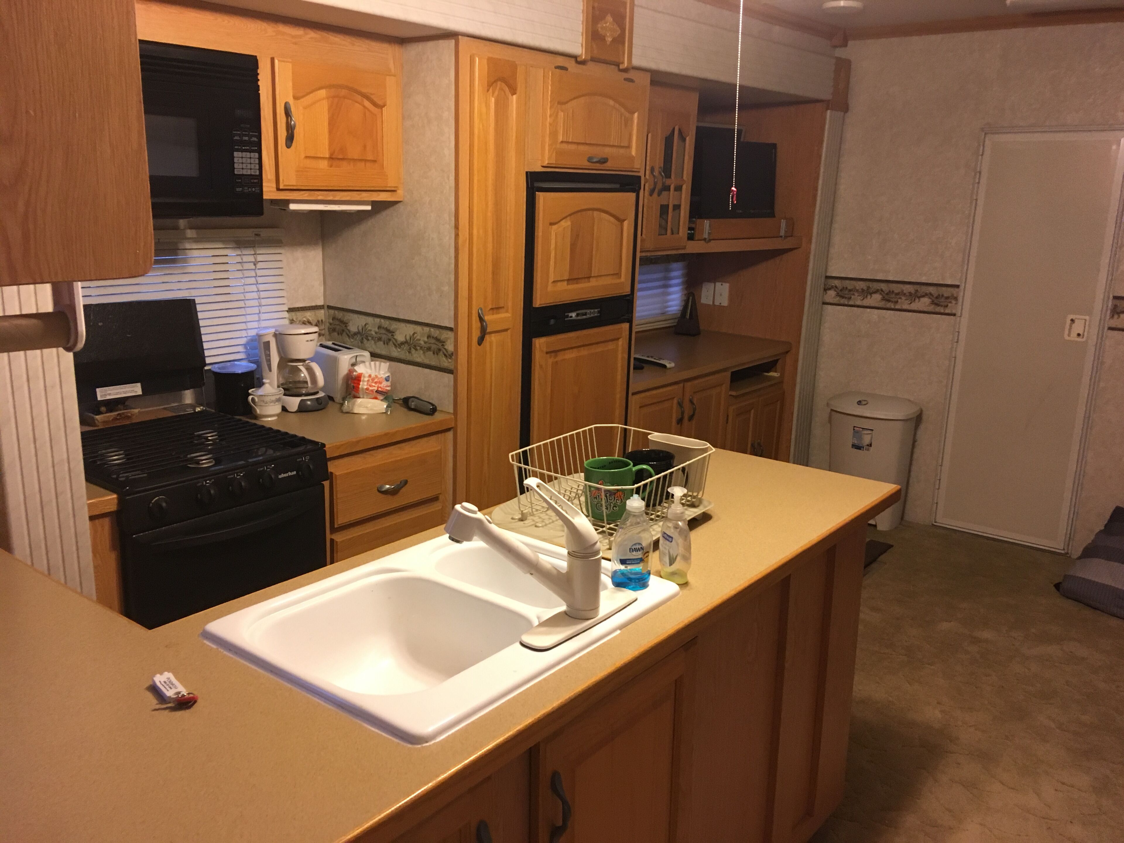 Kitchen area with stove, toaster, microwave, coffee pot, and refrigerator.