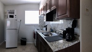 Una cocina compacta con refrigerador, estufa, lavamanos y cafetera.