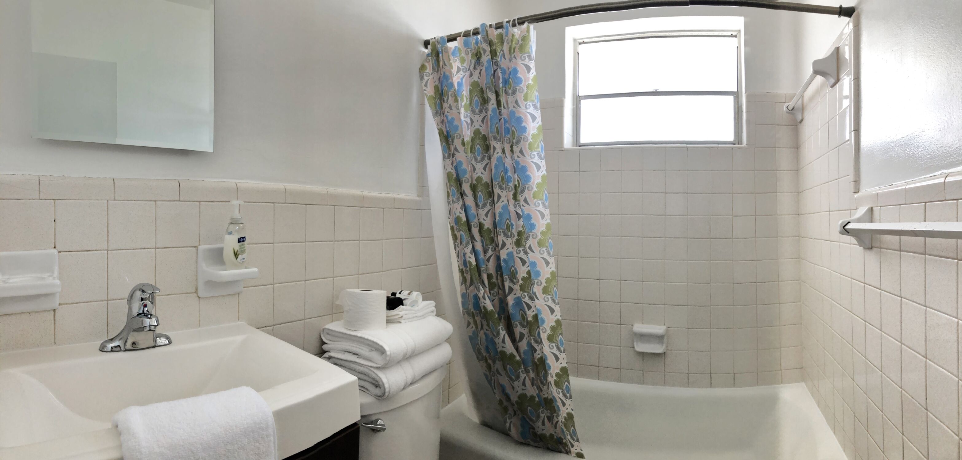 A bathroom with a white sink, a mirror, a toilet, and a shower with a patterned curtain.