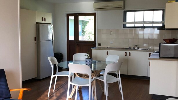 A compact kitchen with white cabinets, a built-in refrigerator, a glass dining table with four chairs, and a window providing natural light. - 9 Indigo Avenue - Rainbow Beach. Close to beach and main street. Walk to everything (RAINBOW BEACH)