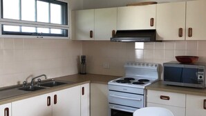 A kitchen with white cabinets, a stove, a microwave, and a sink. - 9 Indigo Avenue - Rainbow Beach. Close to beach and main street. Walk to everything (RAINBOW BEACH)