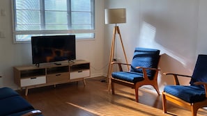 A living room with a TV on a wooden stand, a floor lamp, and two blue chairs.