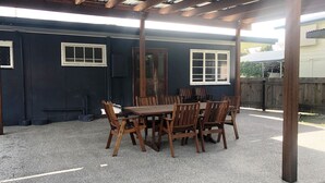 A covered patio with a wooden table and chairs, a dark exterior wall, and a wooden fence in the background. - 9 Indigo Avenue - Rainbow Beach. Close to beach and main street. Walk to everything (RAINBOW BEACH)
