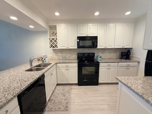 A modern kitchen with white cabinets, a black stove, a microwave, and a coffee maker.