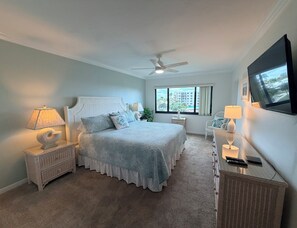 A bedroom with a bed, nightstands, a desk, a chair, a ceiling fan, and a TV.