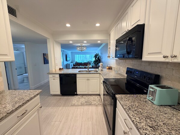 A modern kitchen with white cabinetry, granite countertops, a black stove, and a teal toaster.
