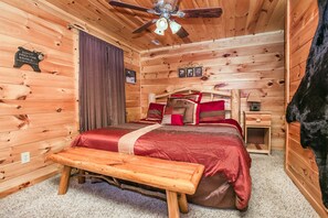Un dormitorio de cabaña de madera con cama, banco, ventilador de techo y paredes de madera.