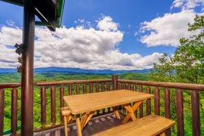 Una terraza de madera con mesa y banco que da a un paisaje montañoso.