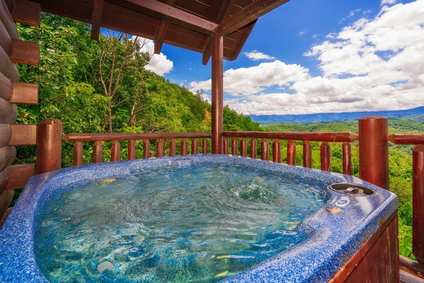 Un jacuzzi con muelle de madera y una vista panorámica de montañas y árboles.