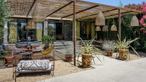 Un espace extérieur abrité, aménagé avec des meubles en osier, des plantes en pot et des lampes suspendues.