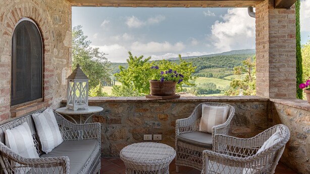 Une terrasse aux murs de pierre, agrémentée de meubles en osier, d’une lanterne et d’une plante en pot.
