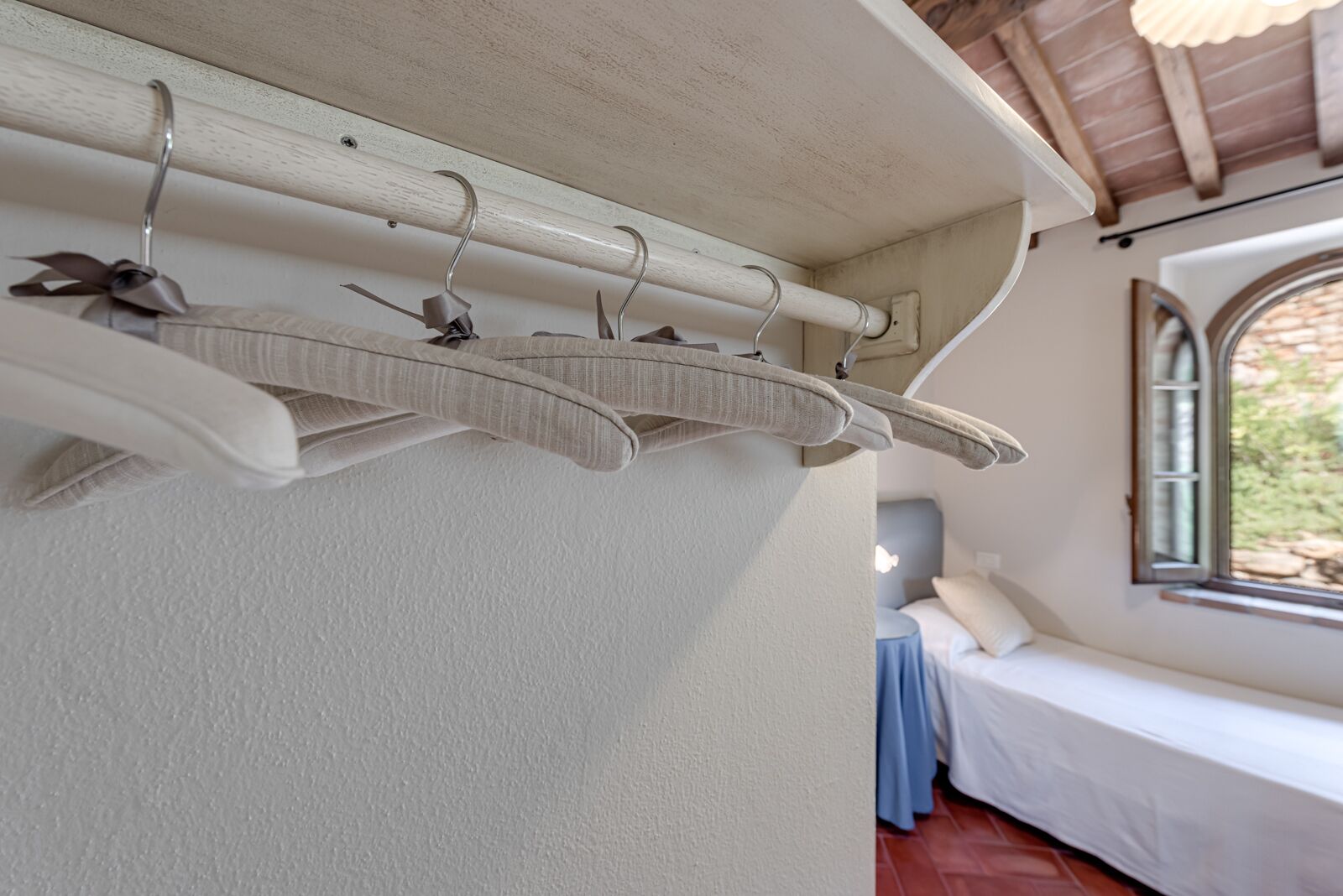 Una habitación con pared blanca, techo de madera, ventana con vistas y cama con cubrecama azul.
