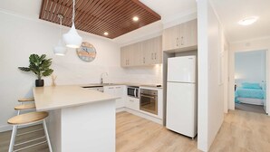 A modern kitchen with white cabinetry, a wooden ceiling, and a central island with stools.