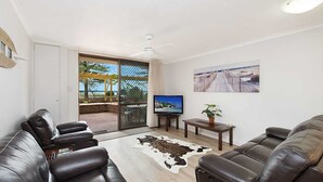 A living room with leather sofas, a TV, a small table with a plant, a cowhide rug, and a view of a beach through a sliding door.