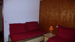A small room with a wooden wall, a red sofa, and a small table with a lamp. - Reberty les Menuires very beautiful 2 rooms facing south (saint martin de belleville)