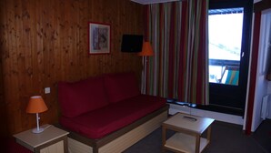 A wooden-paneled room with a red sofa, two small tables, a television, and a window with striped curtains. - Reberty les Menuires very beautiful 2 rooms facing south (saint martin de belleville)