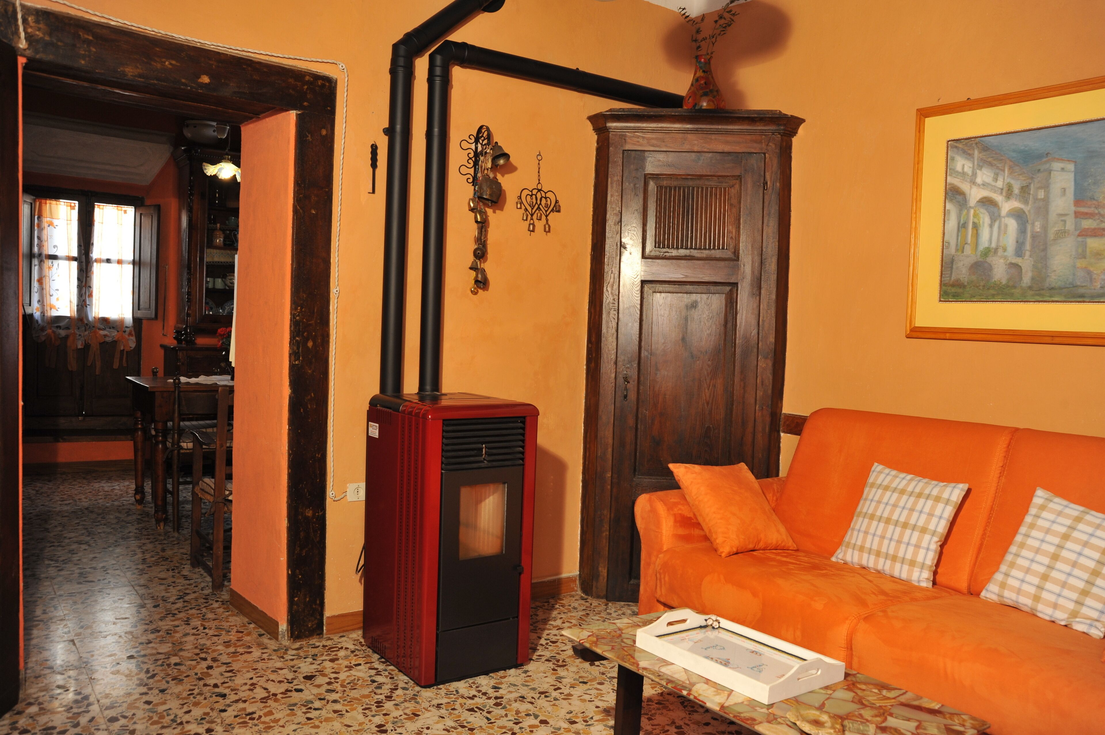 A cozy living room with a red wood-burning stove, an orange sofa, and a wooden cabinet.