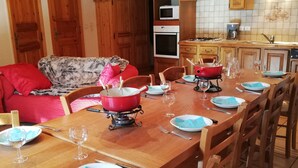 Una mesa de comedor de madera dispuesta con platos, vasos y cubiertos, rodeada de sillas de madera en una cocina con armarios de madera y un microondas.