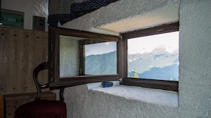 Ein Zimmer mit großem Fenster und Blick auf eine gebirgige Landschaft, ein Holzstuhl und ein Spiegel, der die Aussicht reflektiert.
