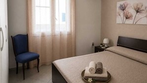 Una habitación de hotel con una cama, una silla, una mesita de noche con lámpara, aire acondicionado y una ventana con cortinas.