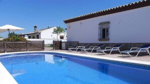Una piscina con sillones de descanso y un edificio blanco de techo con azulejos.