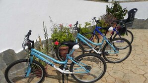 Tres bicicletas estacionadas en un patio de piedra con un muro blanco y algunas plantas al fondo.