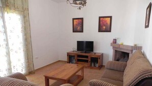 Una sala de estar con un sofá, una mesa de centro de madera, un televisor sobre un mueble de madera y dos cuadros en la pared.