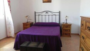 Un dormitorio con una cama individual, dos mesitas de noche, un aparador, un pequeño cofre y un cuadro en la pared.
