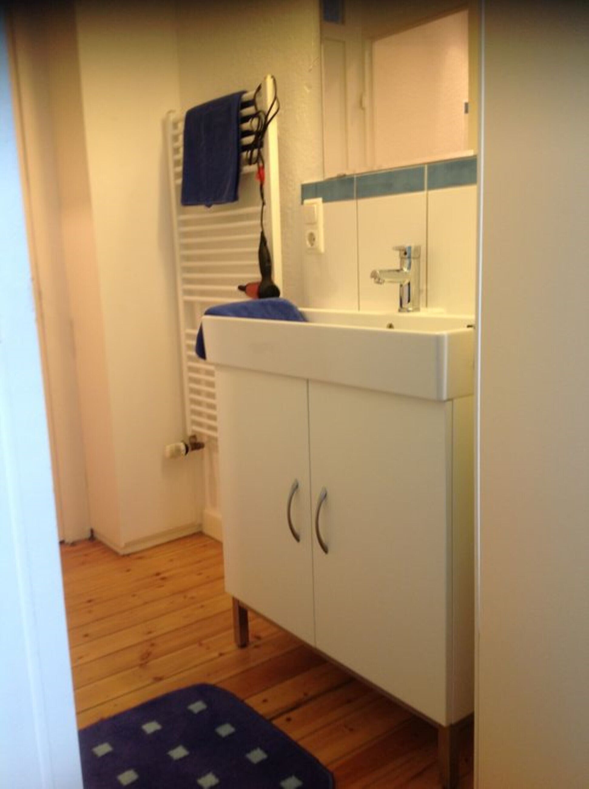 Une salle de bain avec un lavabo blanc, un miroir et un plancher en bois.